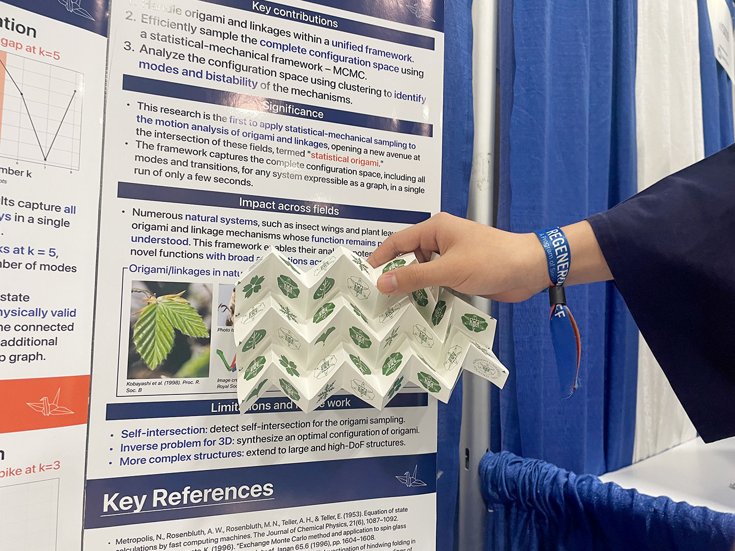 A hand holding an accordion-folded origami structure in front of a science fair research poster about statistical origami and linkage mechanisms, with sections on key contributions, significance, and impact across fields."